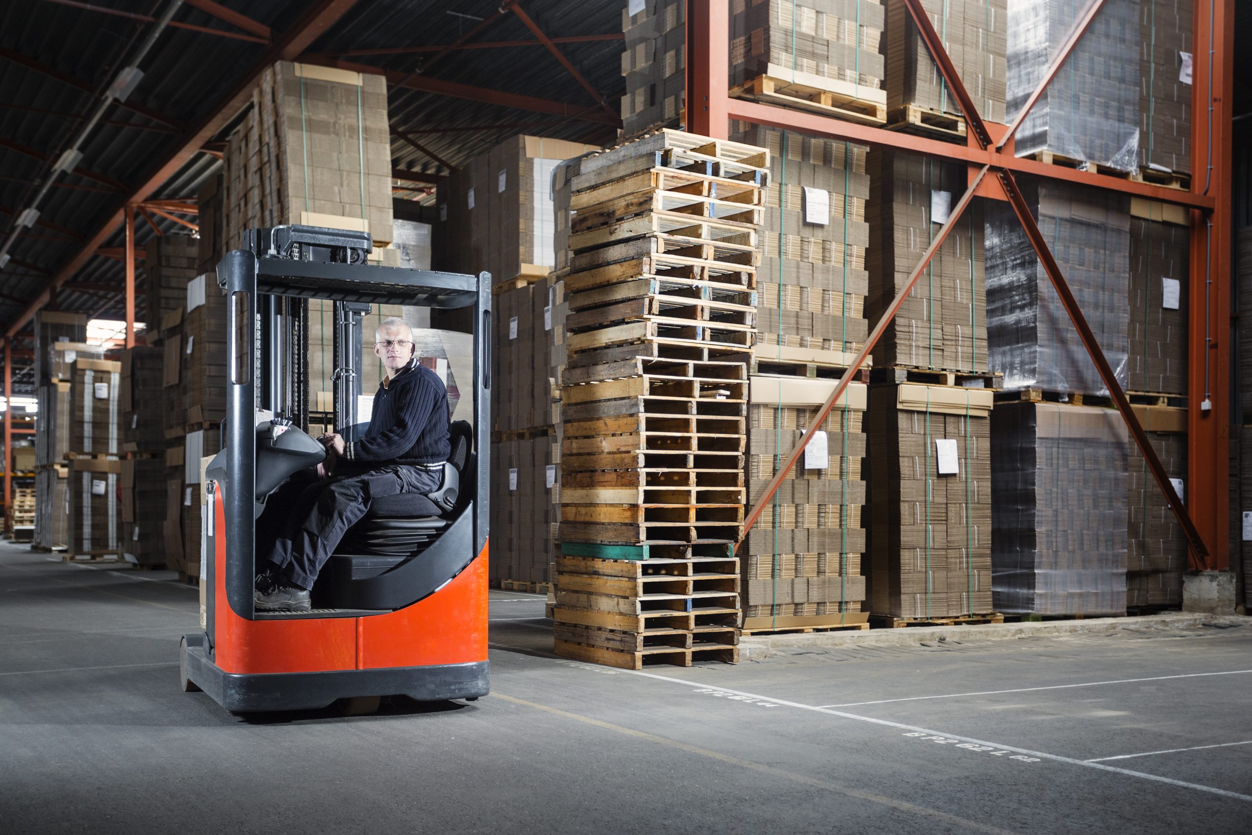 Reach truck driver in a warehouse where pallets and cardboards are stored